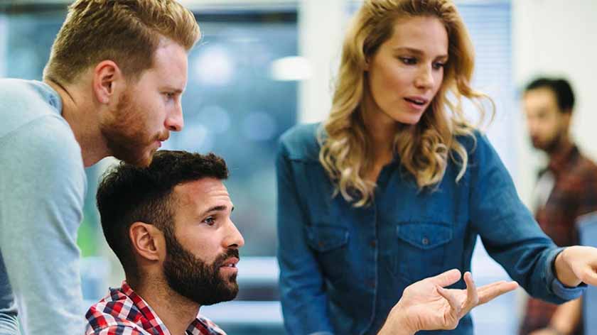 Three coworkers huddled around a computer discussing AI in treasury management
